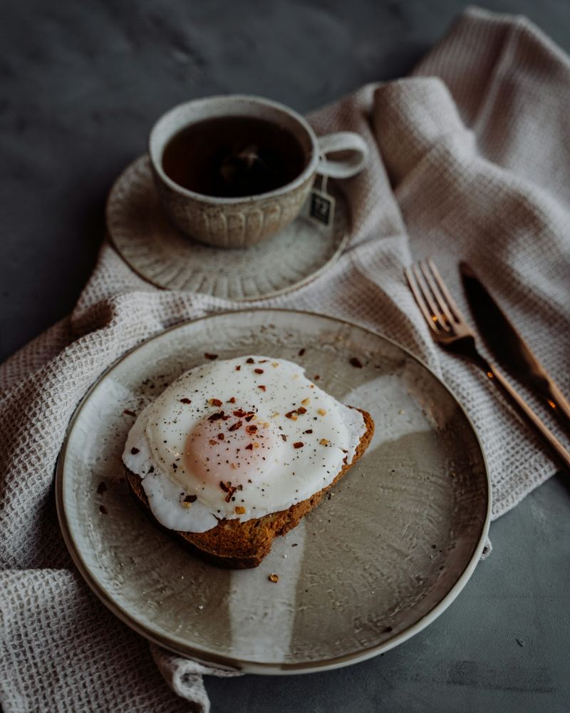 A fried egg on toast with a cup of tea, in morning light