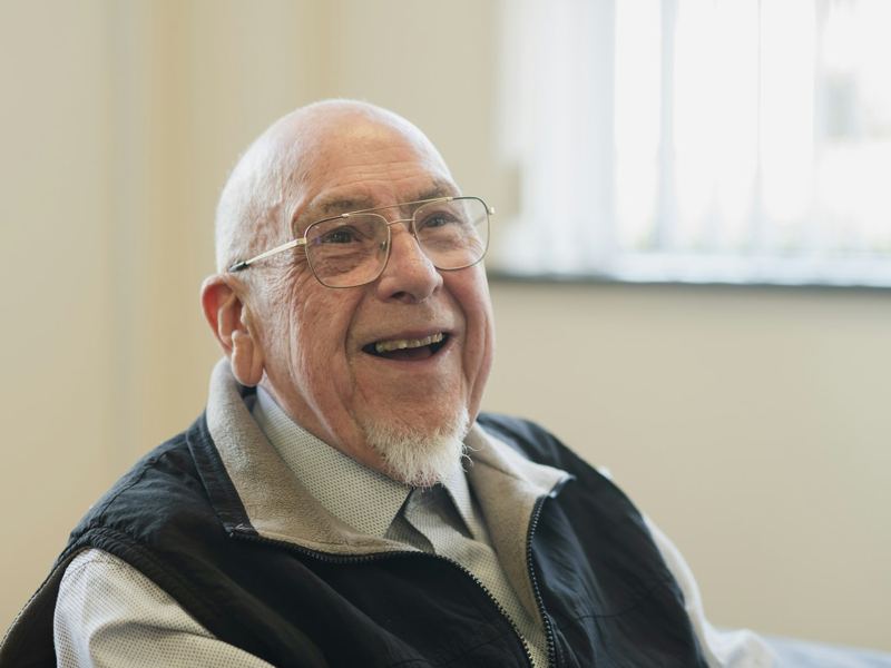 An older man laughing, sitting by a window