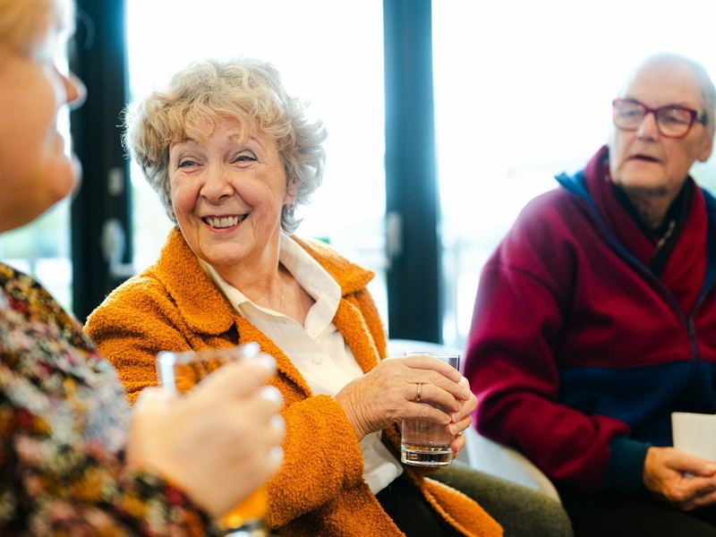 Three older friends talking and laughing together over a drink
